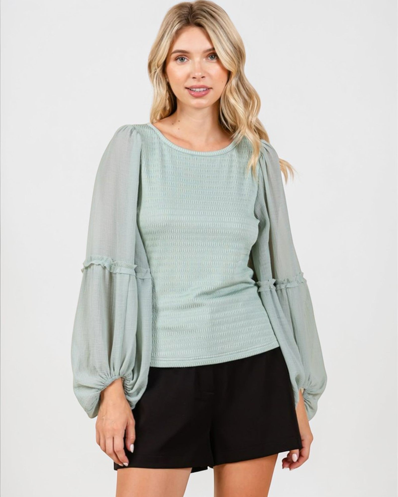 Woman wearing a light blue blouse with sheer sleeves on a white background