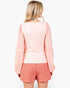 A woman shown from the back wearing a light pink textured long-sleeve top with puffed sleeves and red-and-white checkered shorts against a plain white background.