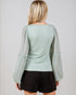 Woman wearing a light green textured top with sheer sleeves against a plain background