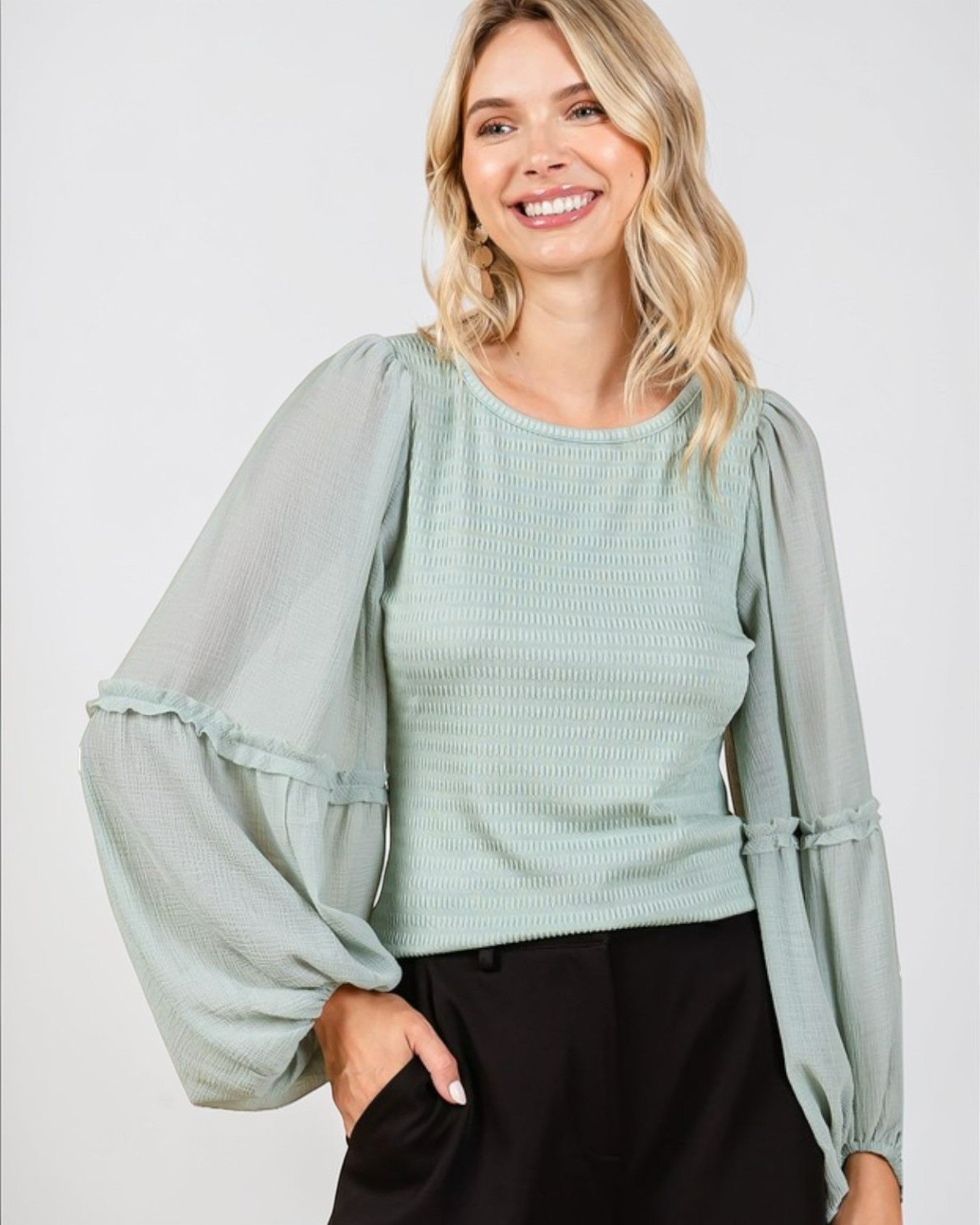 Woman wearing a light green blouse with sheer sleeves on a white background