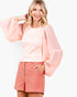 A woman modeling a light pink textured top with dramatic balloon sleeves and matching pink shorts against a plain white background.
