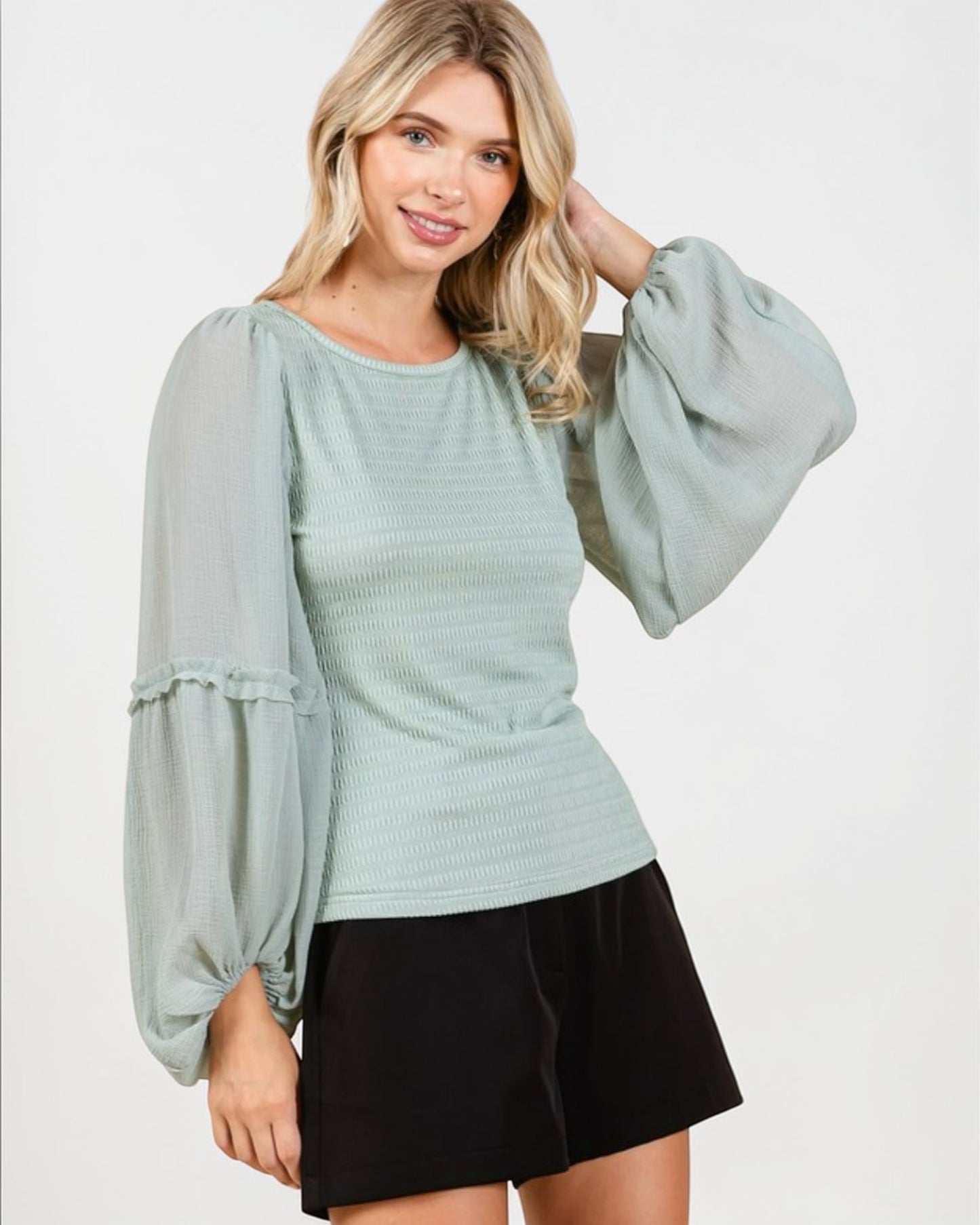 Woman wearing a light blue blouse with puffed sleeves and a black skirt on a white background