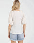 Woman wearing a white lace top and denim shorts on a plain background