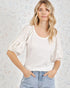 Woman wearing a white textured top and light blue jeans against a light background with abstract patterns.