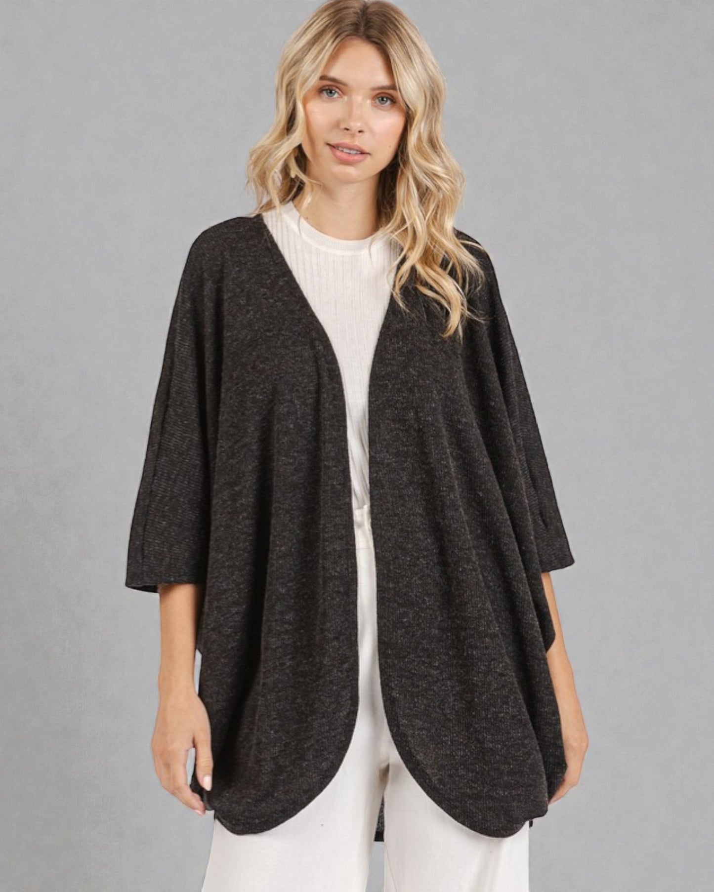 Woman wearing a dark gray cardigan over a white top and pants on a gray background