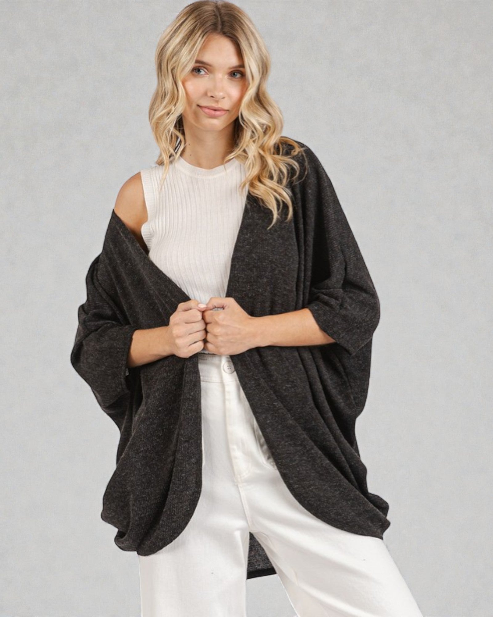 Woman wearing a dark gray poncho over a white outfit on a light gray background