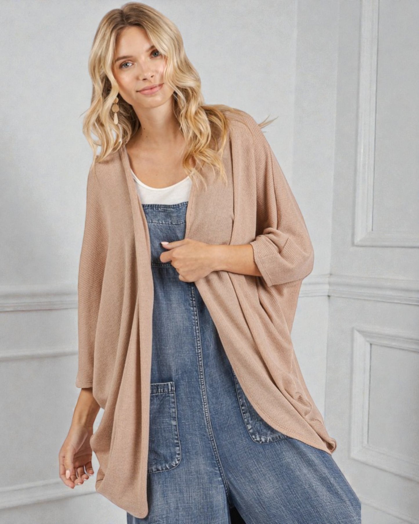 Woman wearing a beige cardigan over a denim dress against a light gray wall.