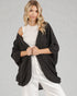 Woman wearing a dark gray poncho over a white outfit on a light gray background