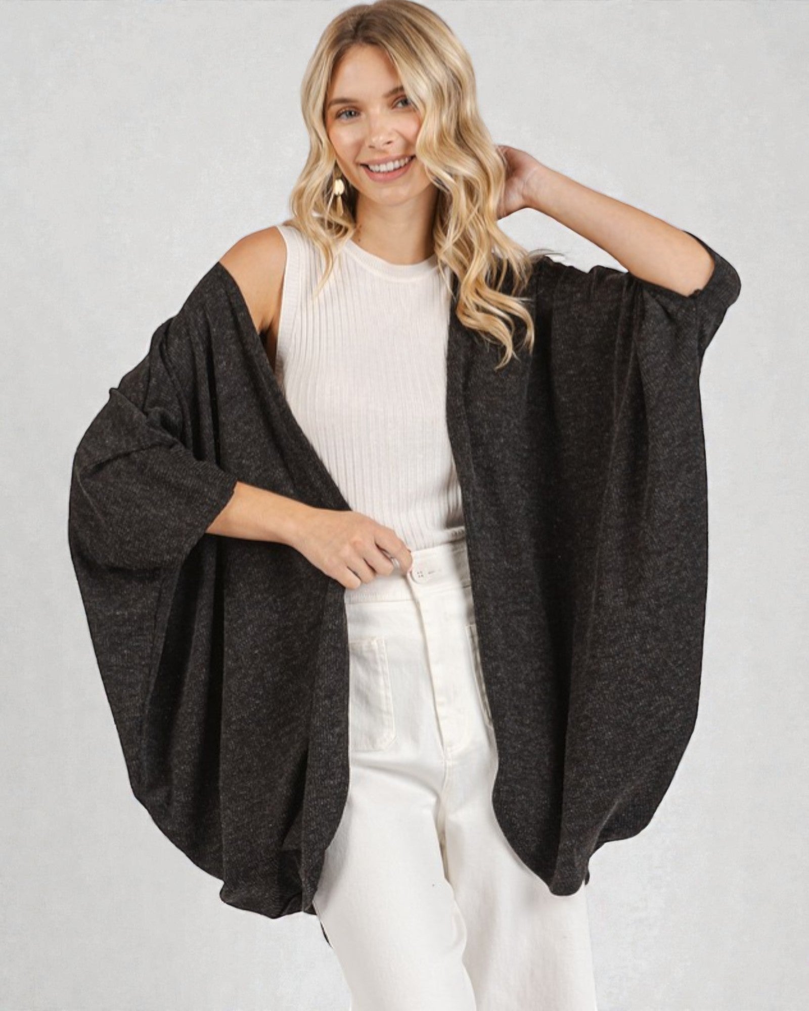 Woman wearing a dark gray cardigan over a white top and pants on a light gray background