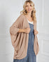 Woman wearing a beige cardigan over a denim dress against a white wall.