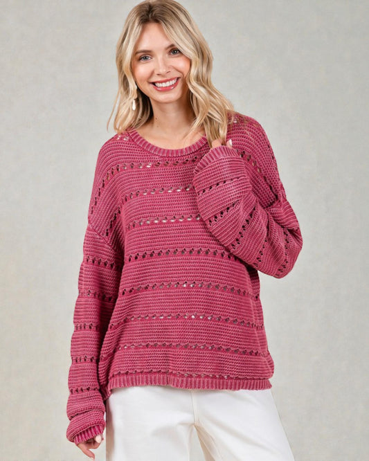 Woman wearing a pink sweater with a subtle pattern on a plain background