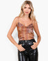 A woman modeling a brown and orange patterned camisole top with thin straps, paired with black faux-leather pants, against a plain white background.