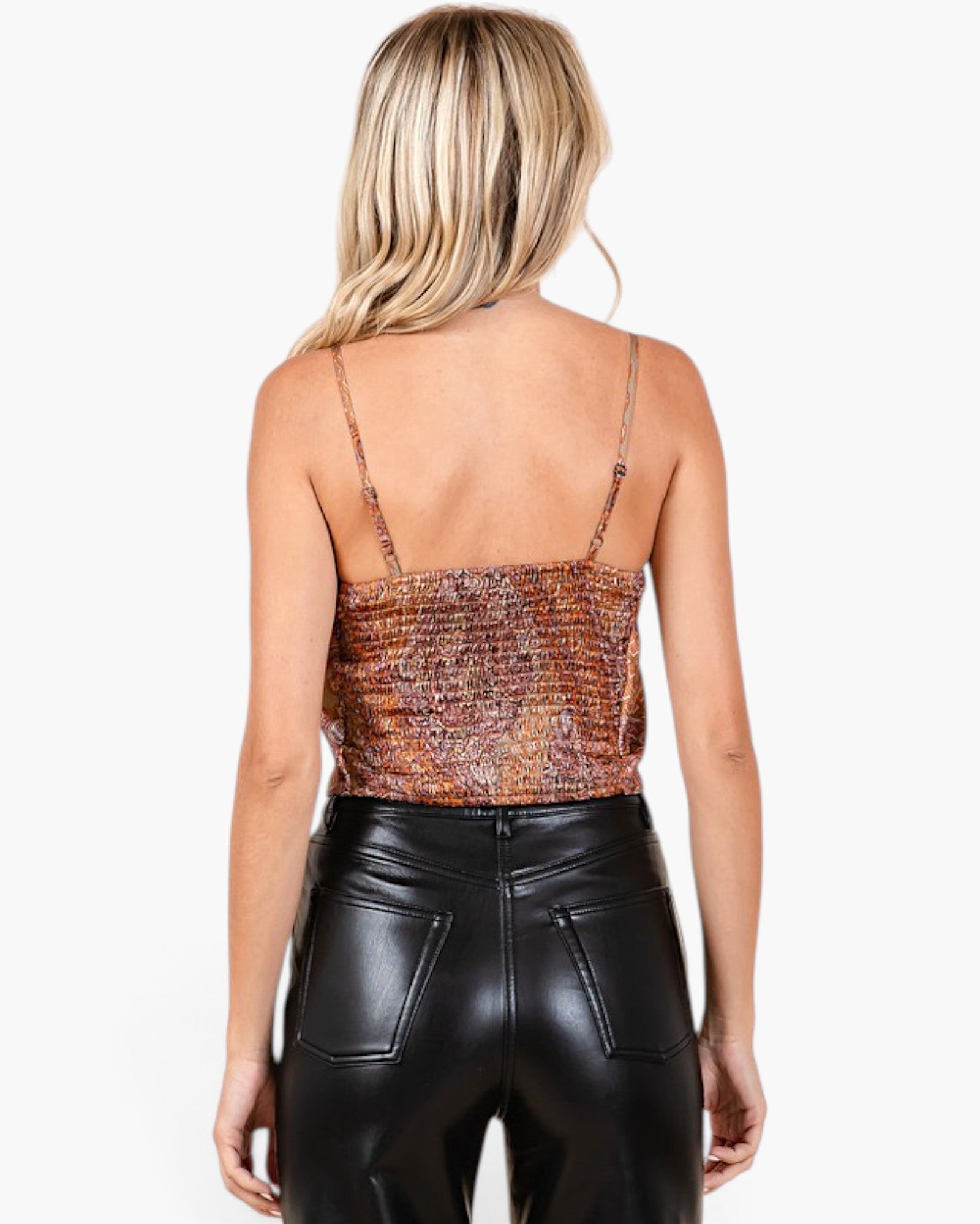 A woman shown from the back wearing a textured, snakeskin-patterned spaghetti-strap top and black faux-leather pants, against a plain white studio background.