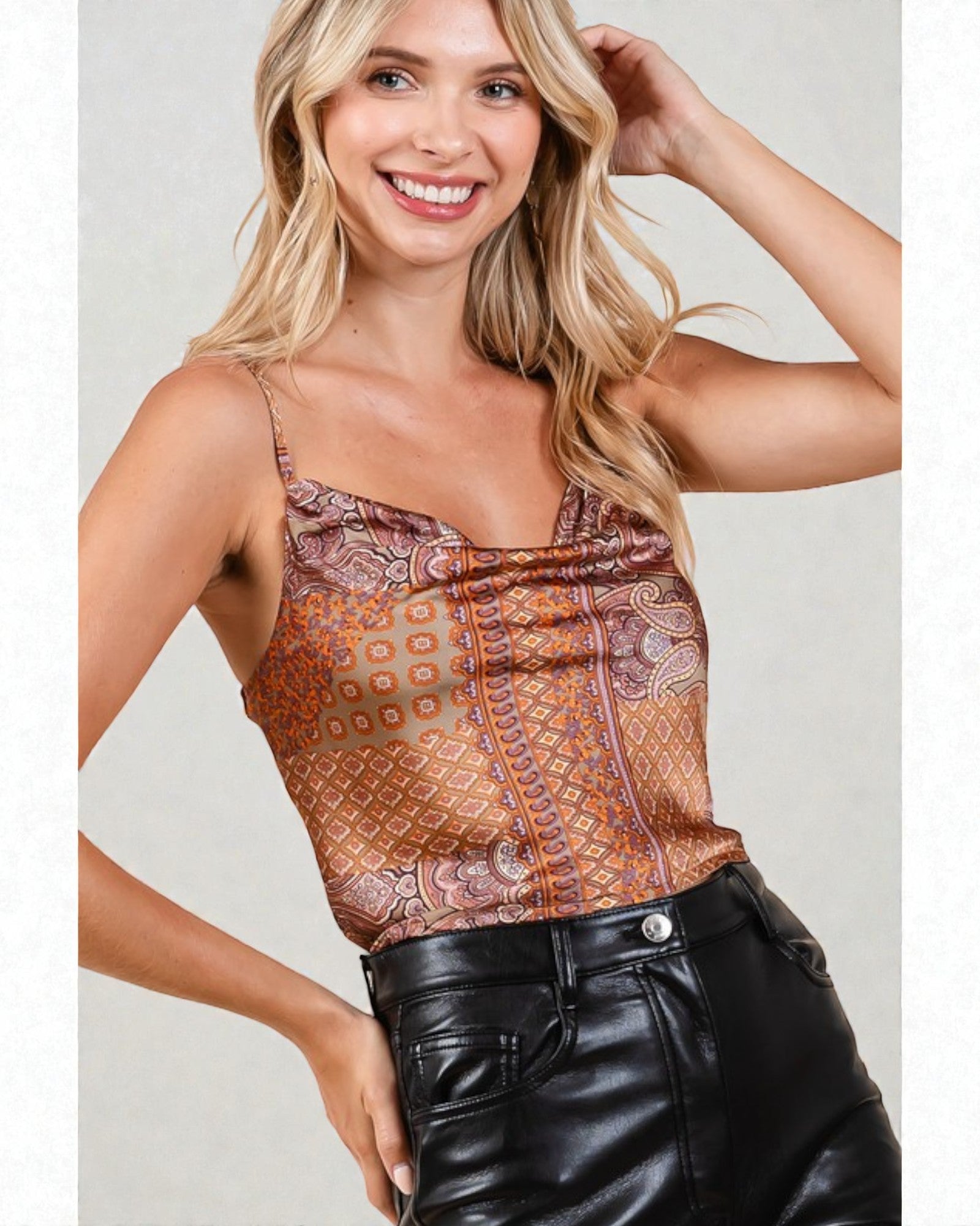 Woman wearing a patterned orange top and black leather pants on a plain background