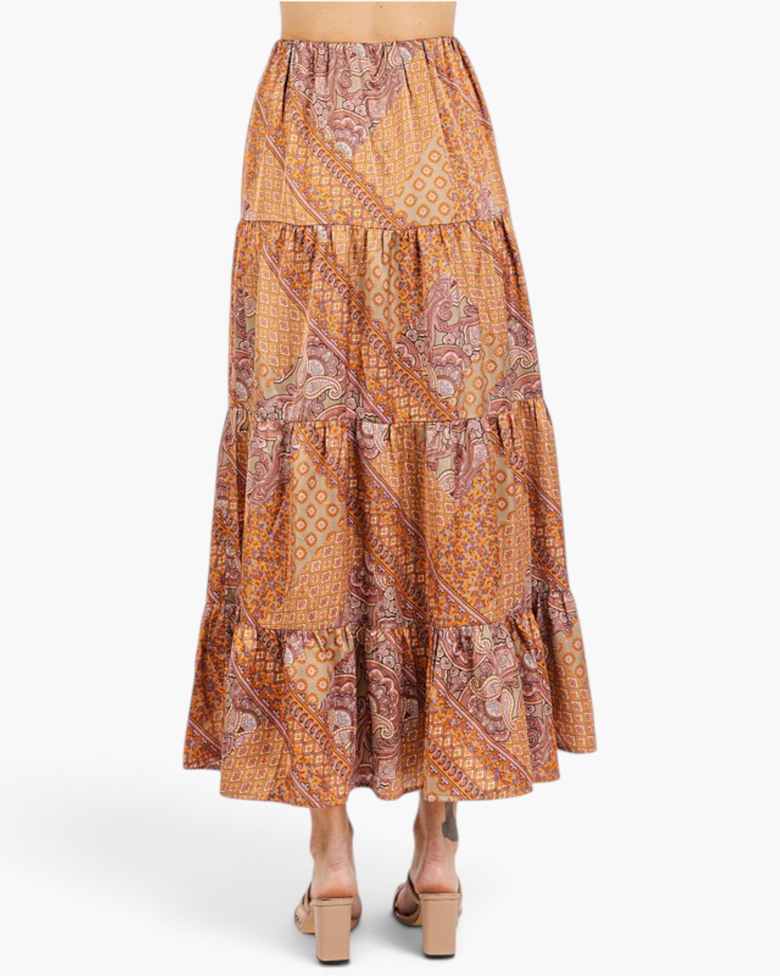 A tiered maxi skirt with an intricate orange, brown, and beige paisley and geometric pattern, shown on a model from the back against a light gray studio background.
