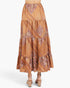 A tiered maxi skirt with an intricate orange, brown, and beige paisley and geometric pattern, shown on a model from the back against a light gray studio background.
