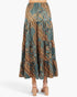 A tiered maxi skirt with a complex batik-style pattern in teal, brown, and gold, shown from the back on a model wearing beige block-heel sandals against a light gray background.