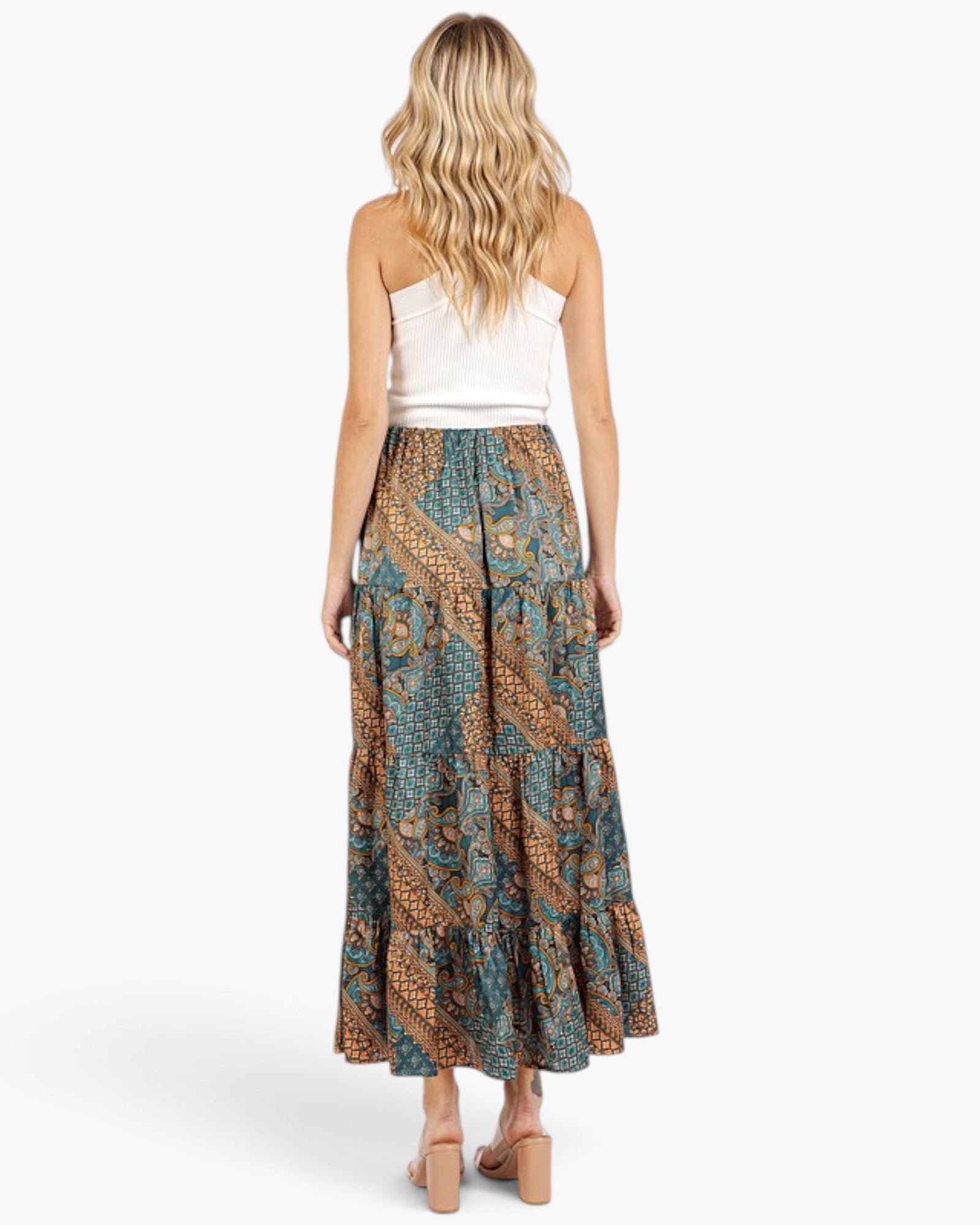 A woman shown from the back wearing a white strapless top and a long tiered maxi skirt with a teal, brown, and gold paisley pattern, standing against a light gray studio background.