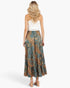A woman shown from the back wearing a white strapless top and a long tiered maxi skirt with a teal, brown, and gold paisley pattern, standing against a light gray studio background.