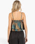 A woman shown from the back wearing a patterned camisole top with thin straps and a ruffled layered hem, paired with black wide-leg pants, against a plain white studio background.