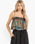 A woman modeling a sleeveless ruffled top with a blue, gold, and brown paisley pattern, paired with black wide-leg pants, against a plain white background.