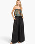 A woman modeling a sleeveless ruffled top with a blue, gold, and brown paisley pattern, paired with wide-leg black pants, against a light gray studio background.