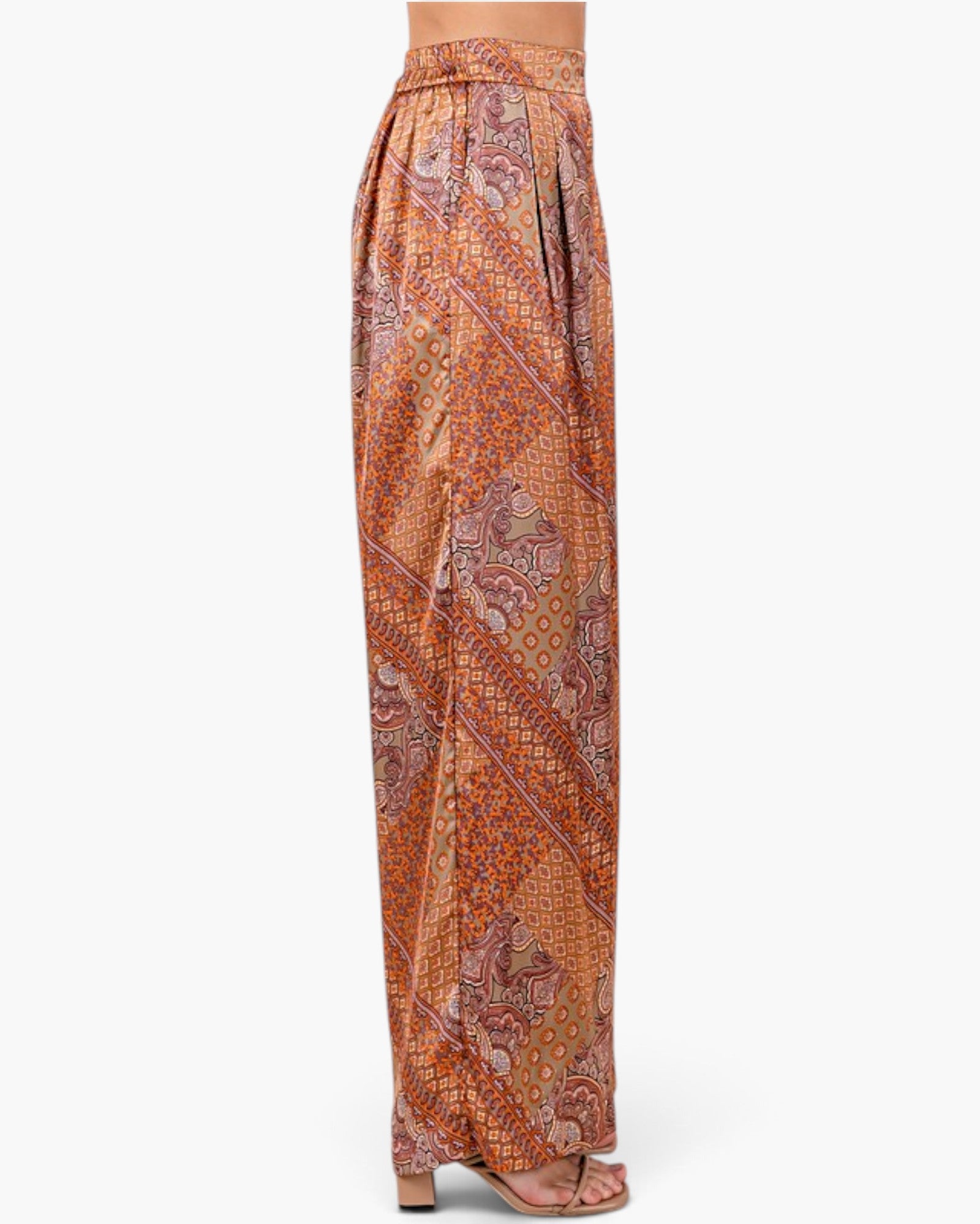A pair of wide-leg trousers with a complex paisley and geometric pattern in orange, brown, and beige, shown on a model from the waist down against a light gray background.