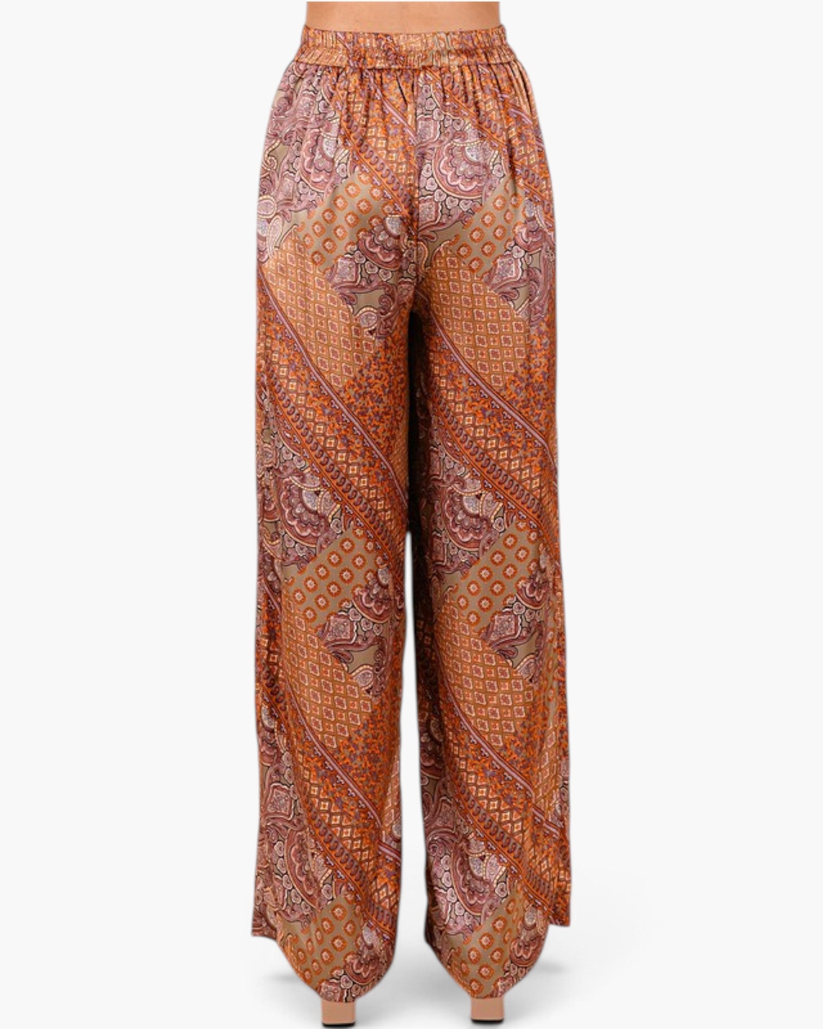 A pair of wide-leg pants with an intricate orange, brown, and beige paisley and geometric pattern, shown on a model from the waist down against a light gray background.