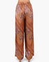 A pair of wide-leg pants with an intricate orange, brown, and beige paisley and geometric pattern, shown on a model from the waist down against a light gray background.