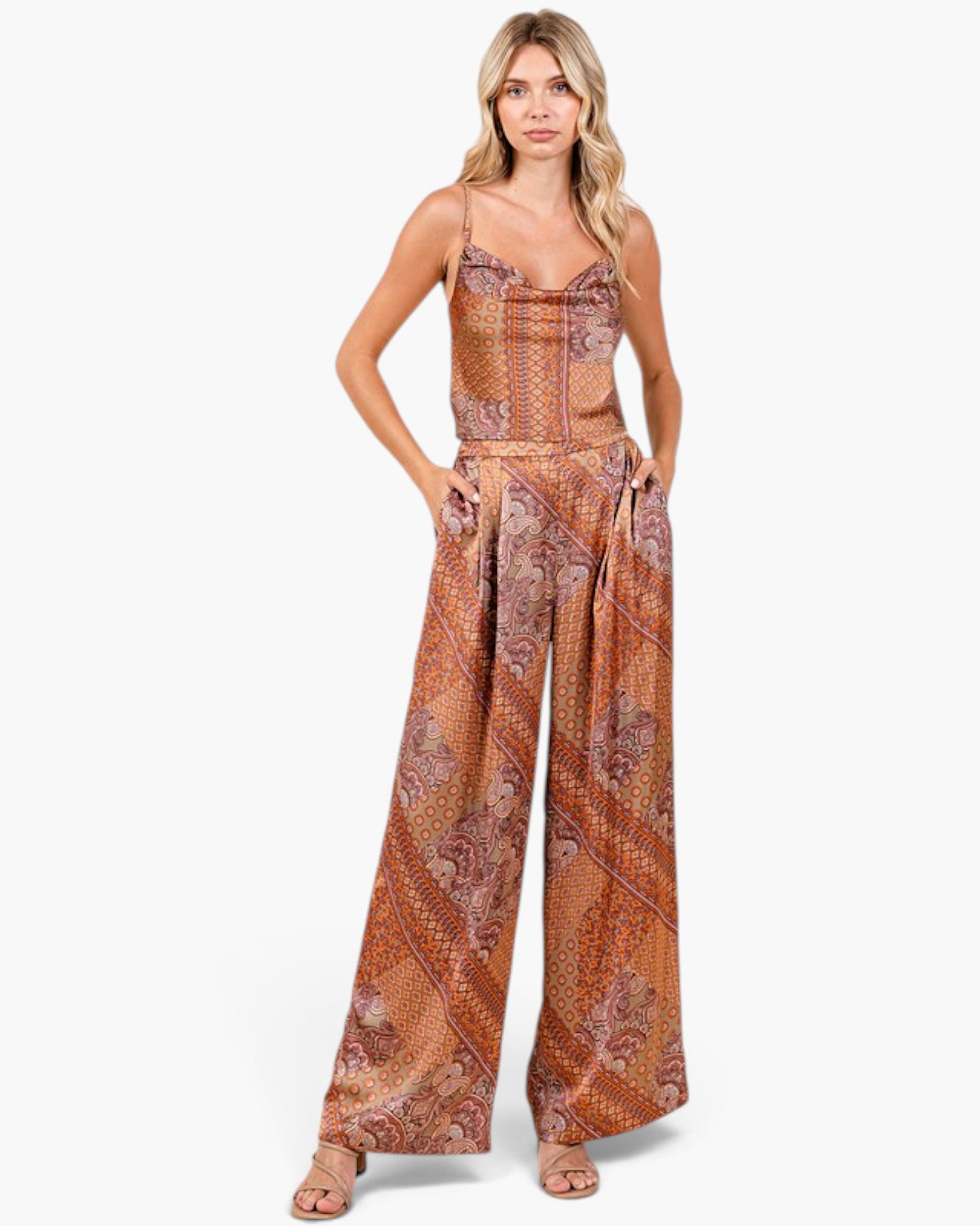 A woman modeling a sleeveless wide-leg jumpsuit with a rust-orange and brown paisley pattern, photographed against a clean white studio background.