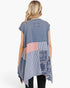 A woman viewed from the back wearing a sleeveless patchwork tunic top. The top has a faded blue-gray base with a central patchwork panel featuring gingham, coral check, and blue bandana patterns.