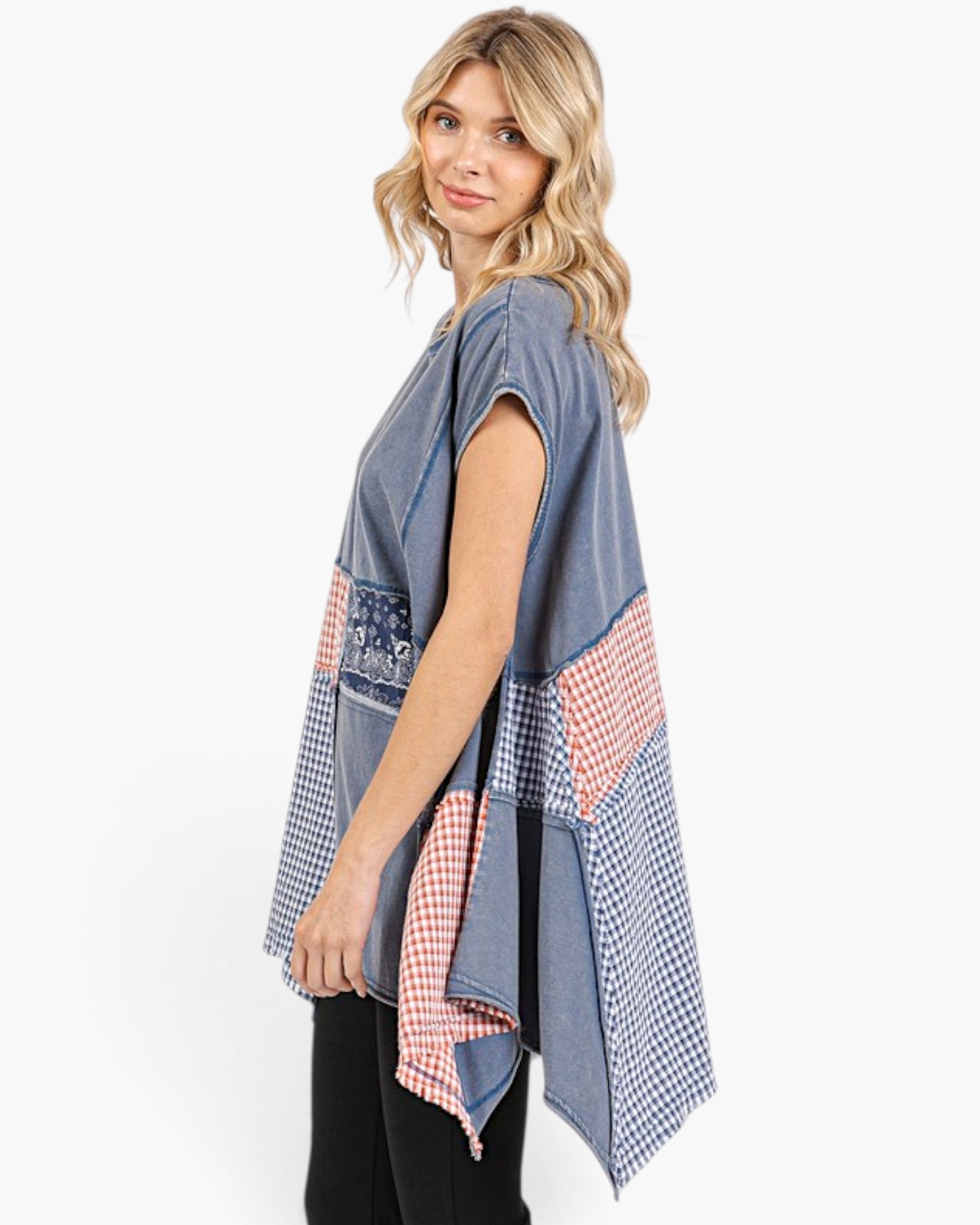 A woman modeling a sleeveless patchwork poncho top with blue denim-like fabric and red-and-white gingham patterned panels, shown against a plain light gray studio background.