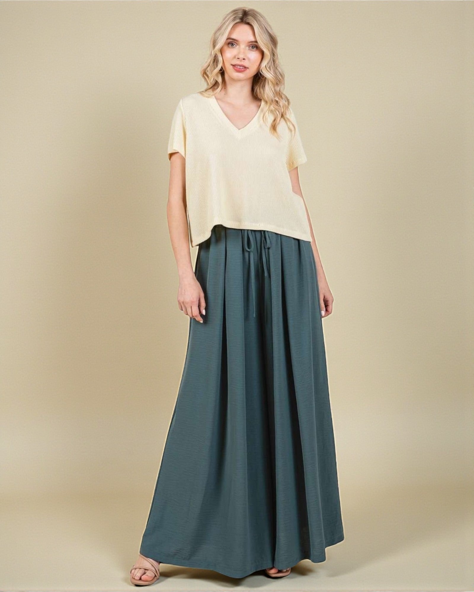 Woman wearing a light yellow top and teal skirt on a beige background