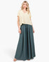 A woman modeling a cream short-sleeve V-neck top and dark teal wide-leg pleated pants against a plain white studio background.