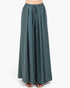 A person wearing a pair of wide-leg, floor-length pleated pants in a muted teal-green color, styled with brown strappy flat sandals against a plain light gray studio background.