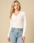 Woman wearing a white long-sleeve shirt and light blue jeans against a beige background