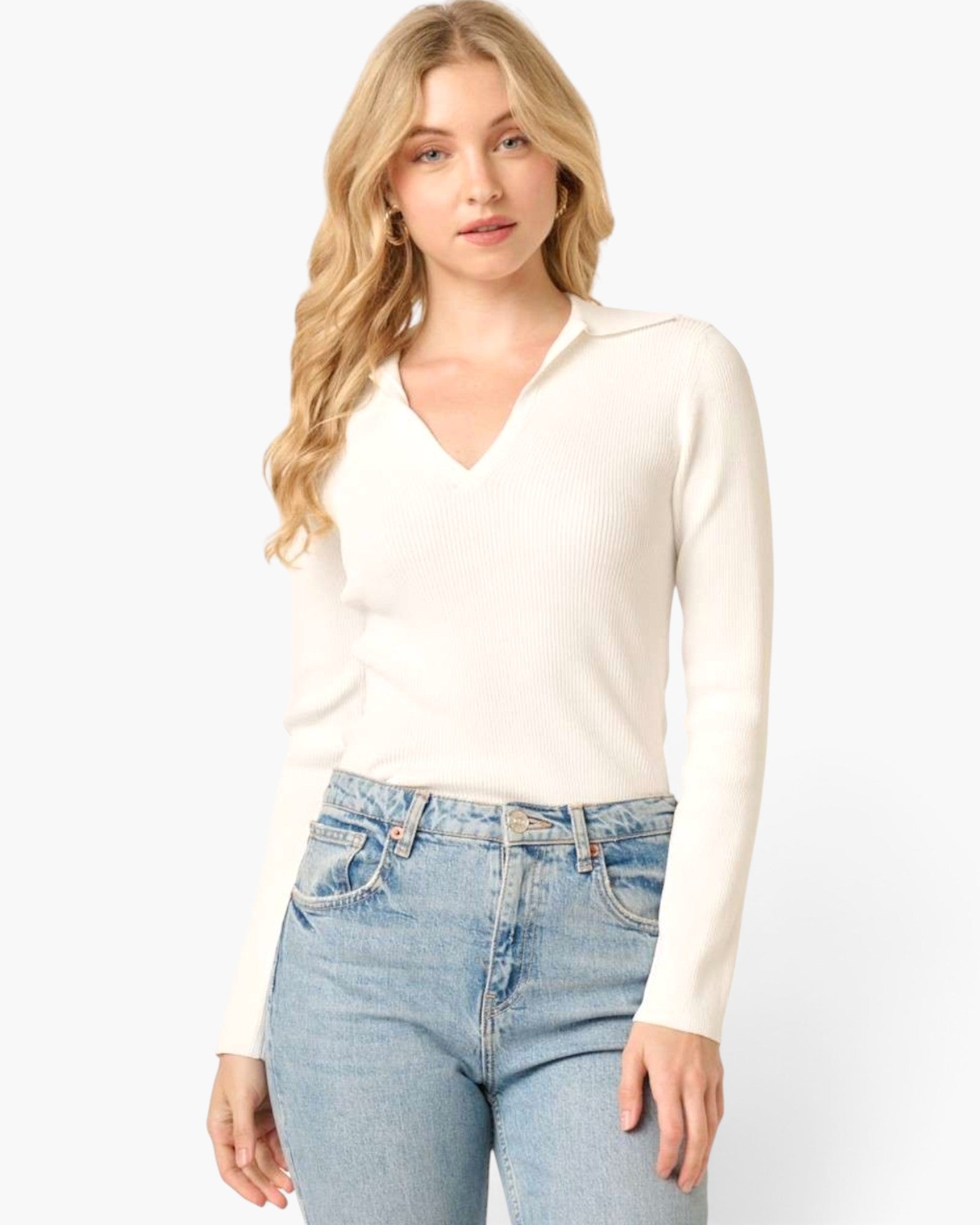 A woman modeling a cream ribbed long-sleeve V-neck knit top with light-wash blue jeans against a plain white studio background.