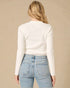 Person wearing a white long-sleeve top and light blue jeans on a beige background