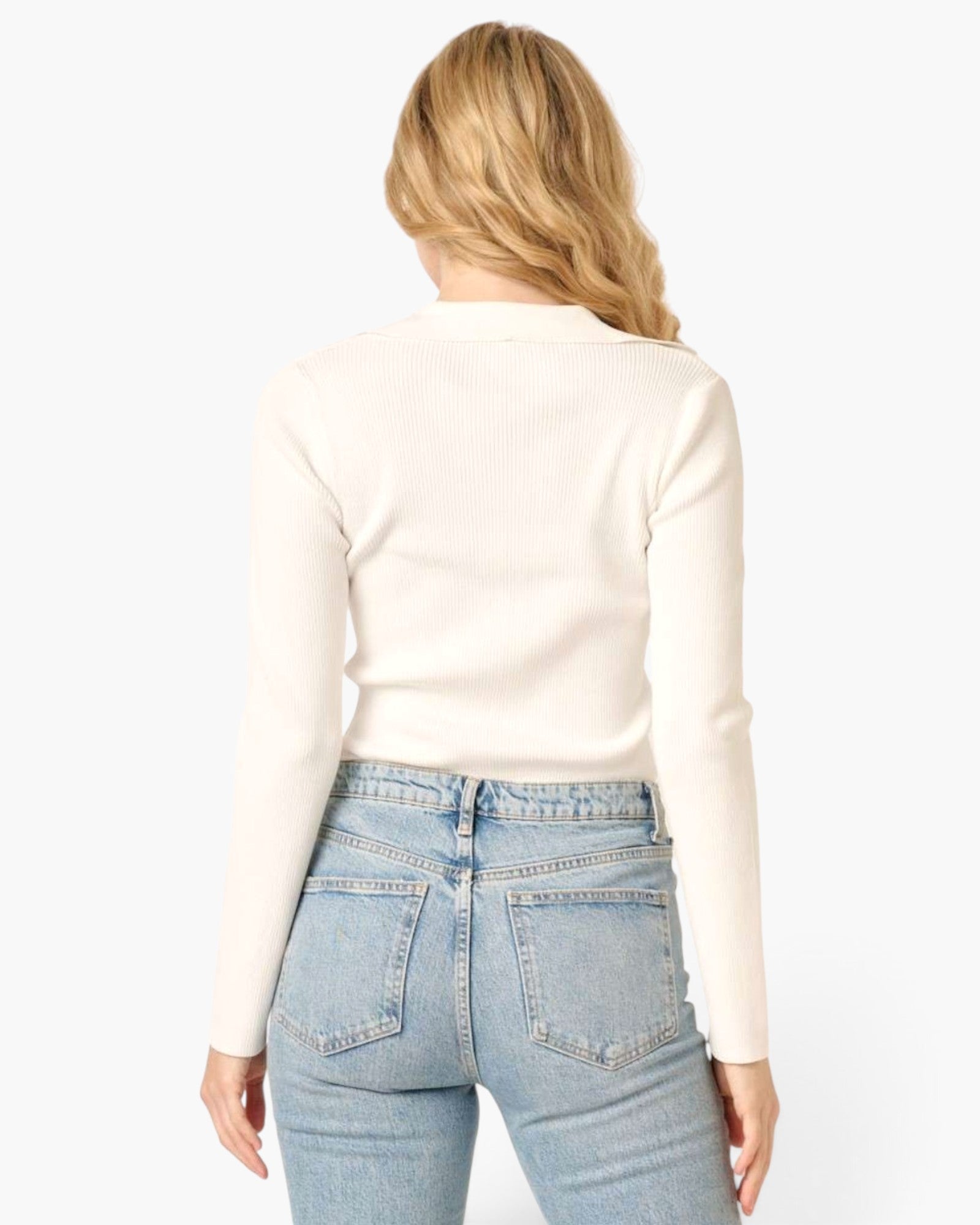 A woman shown from the back wearing a fitted cream ribbed long-sleeve top and light blue jeans against a plain light gray studio background.