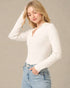 Woman wearing a white long-sleeve top and blue jeans against a beige background