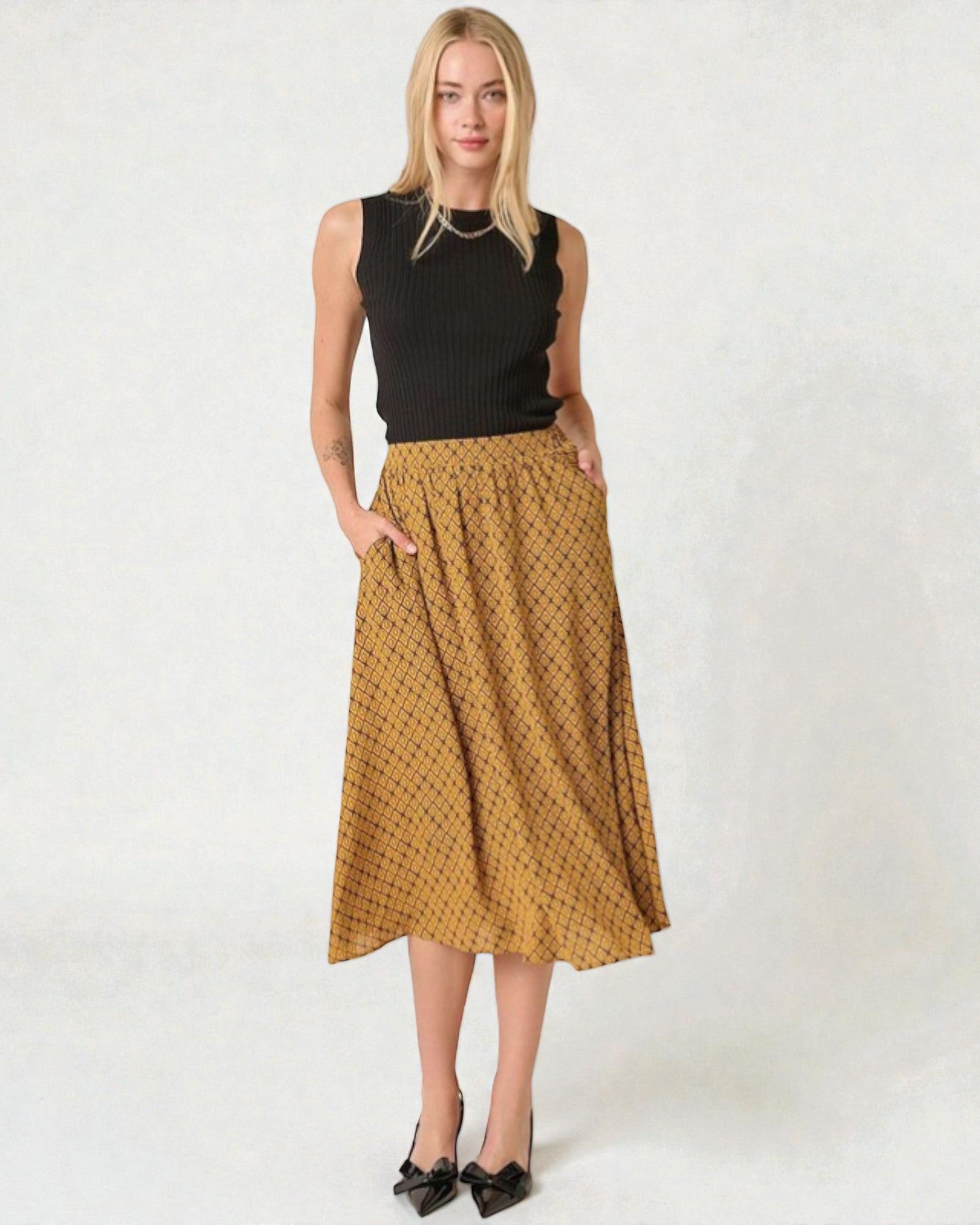 Woman wearing a black top and mustard yellow patterned skirt on a white background