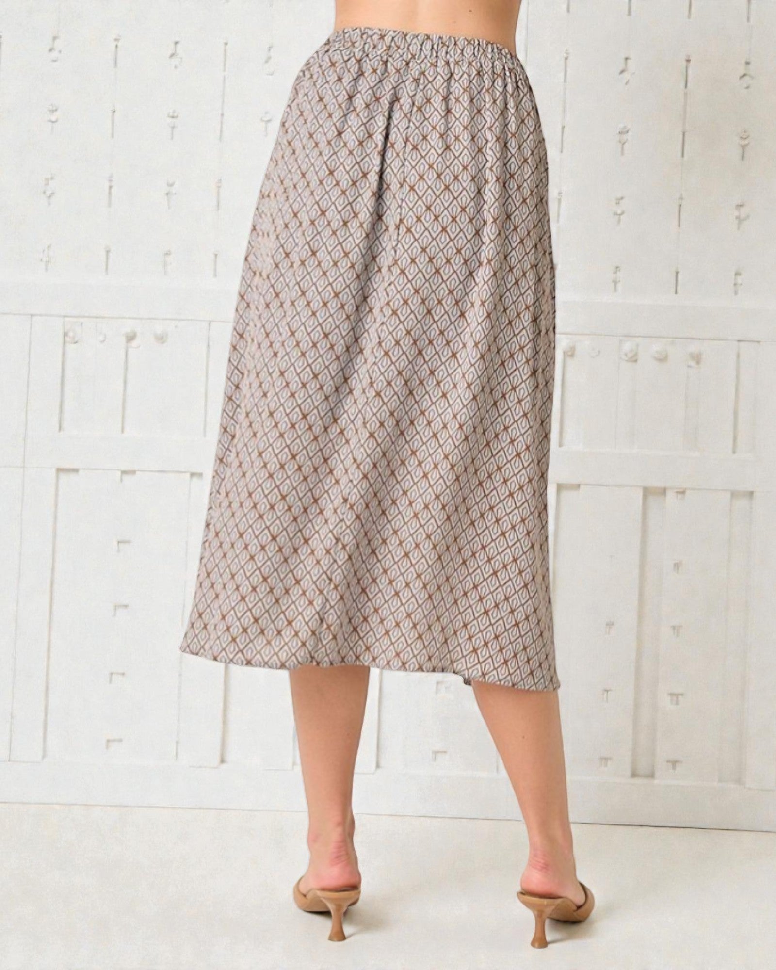 Person wearing a patterned skirt against a white wooden panel background