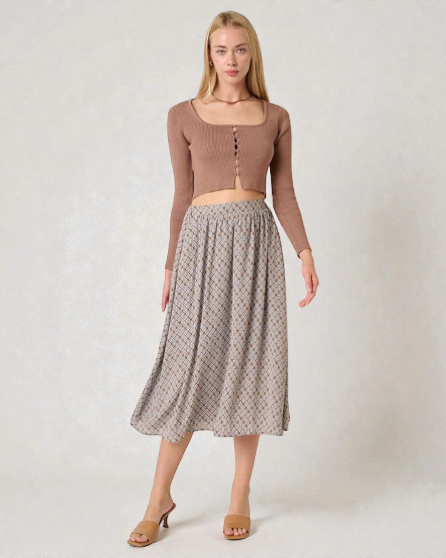 Woman wearing a brown long-sleeve top and patterned skirt on a white background