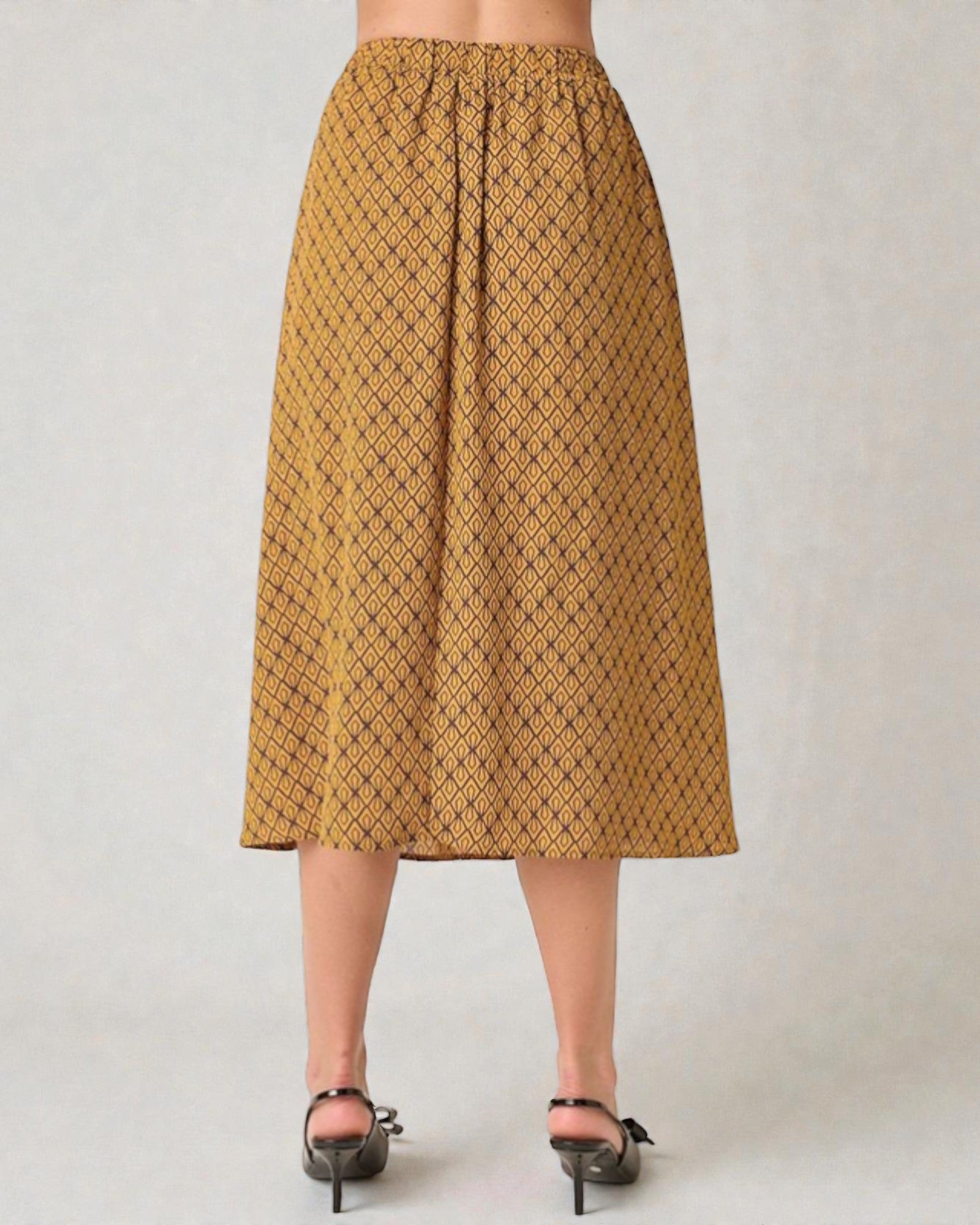 Person wearing a mustard yellow patterned skirt on a plain background