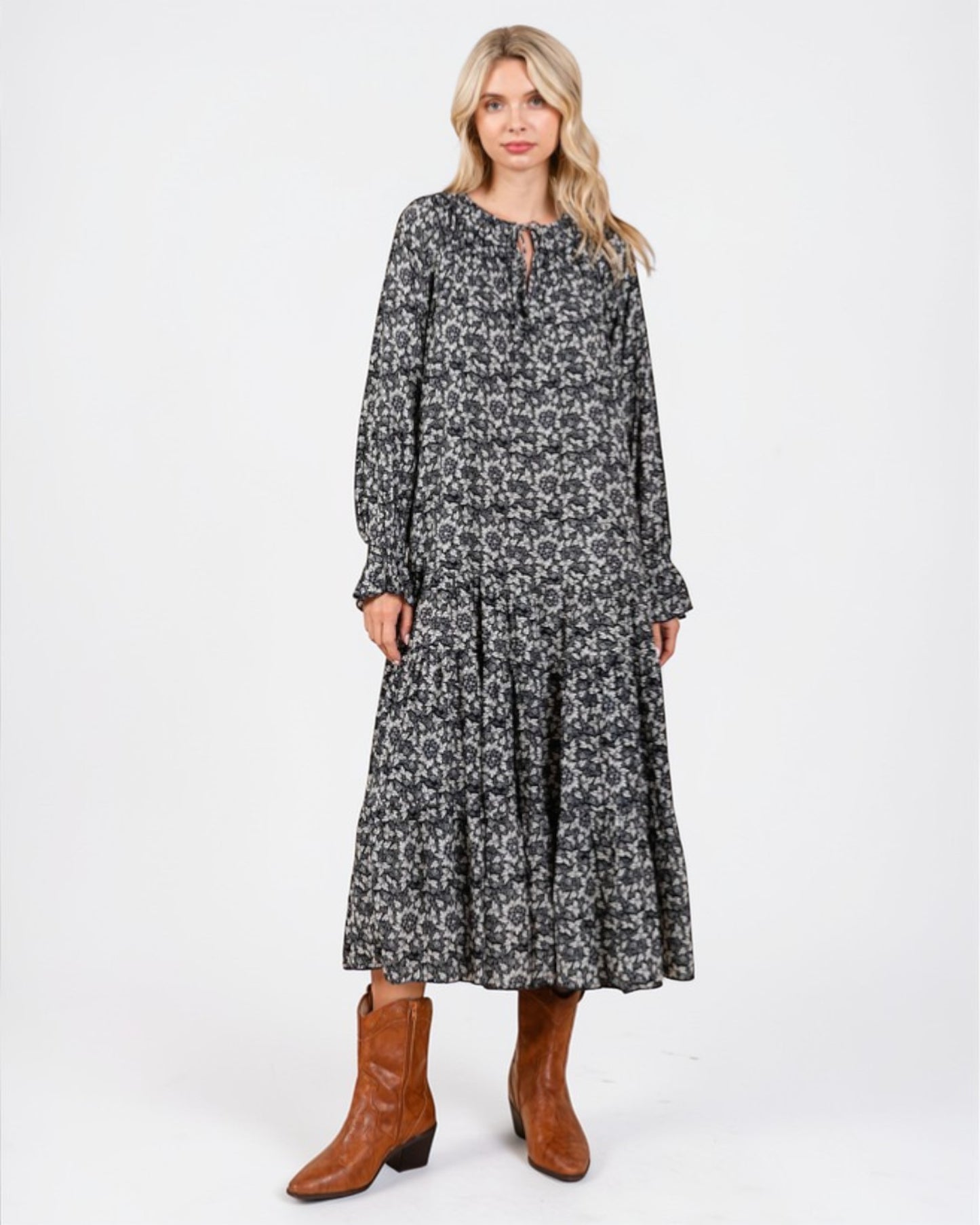 Woman wearing a black floral dress with brown boots on a white background