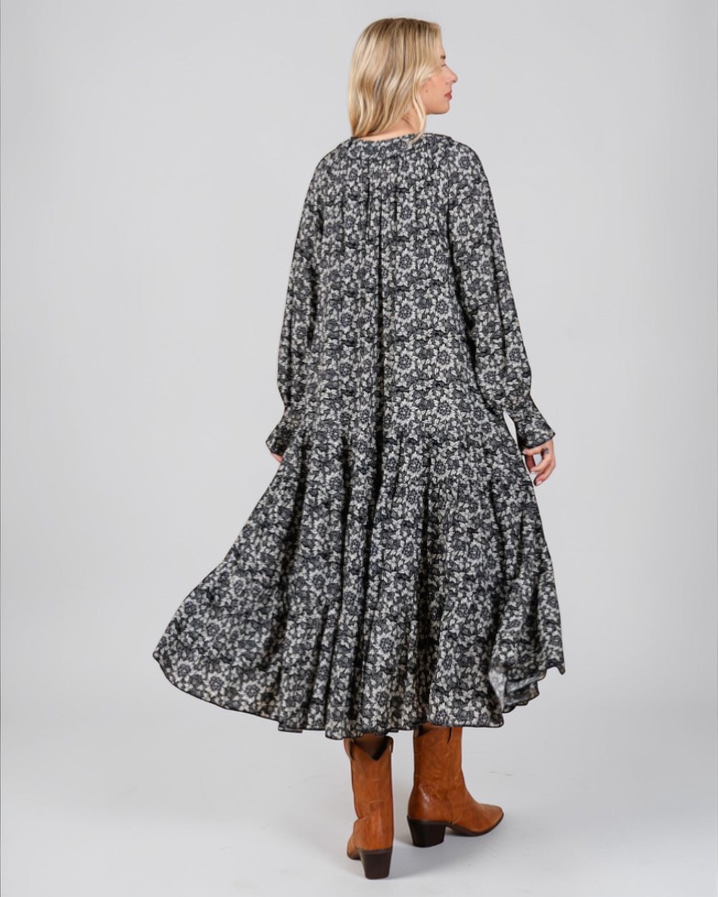 Woman wearing a long, patterned dress with brown boots on a plain background