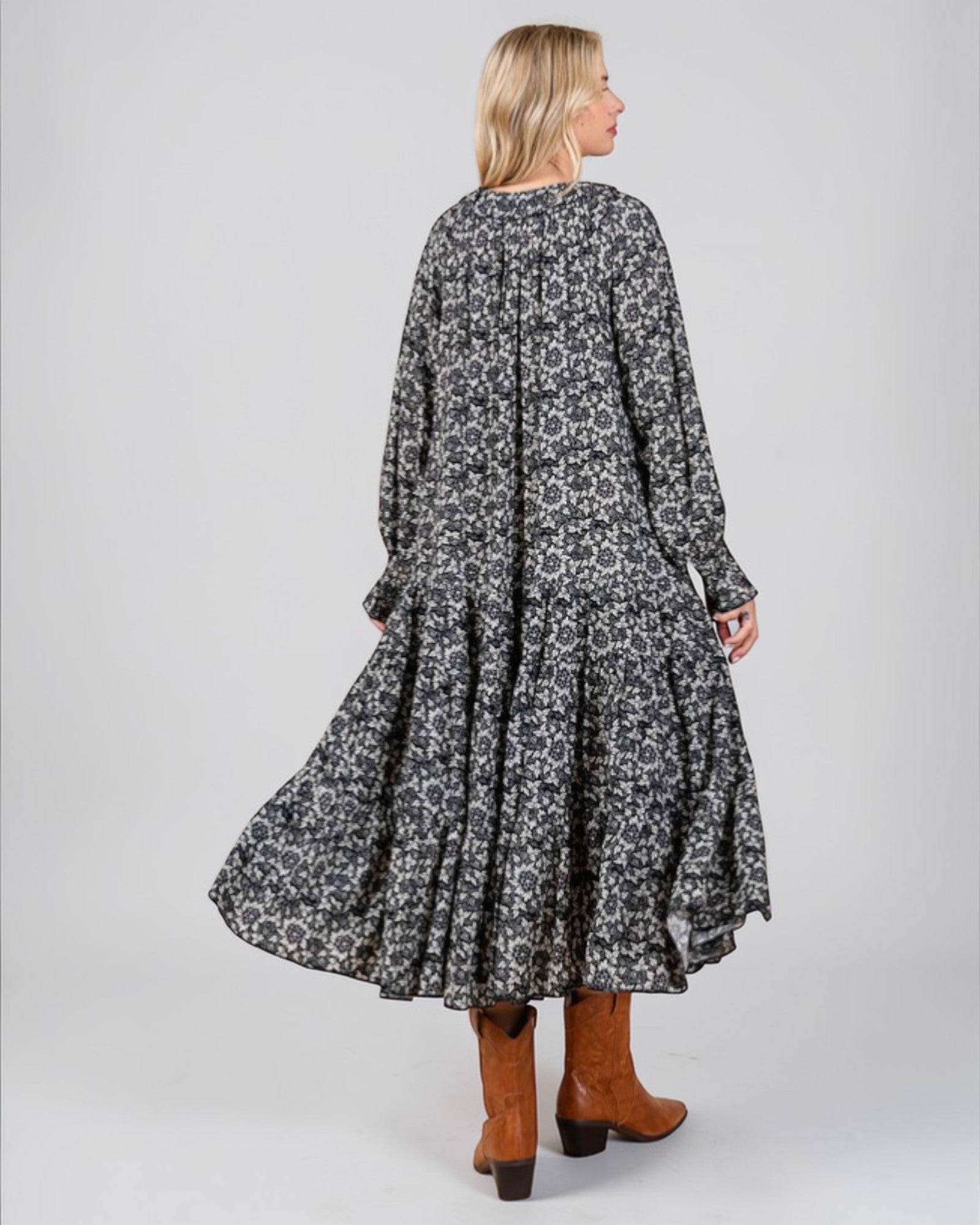 Woman wearing a long, patterned dress with brown boots on a plain background