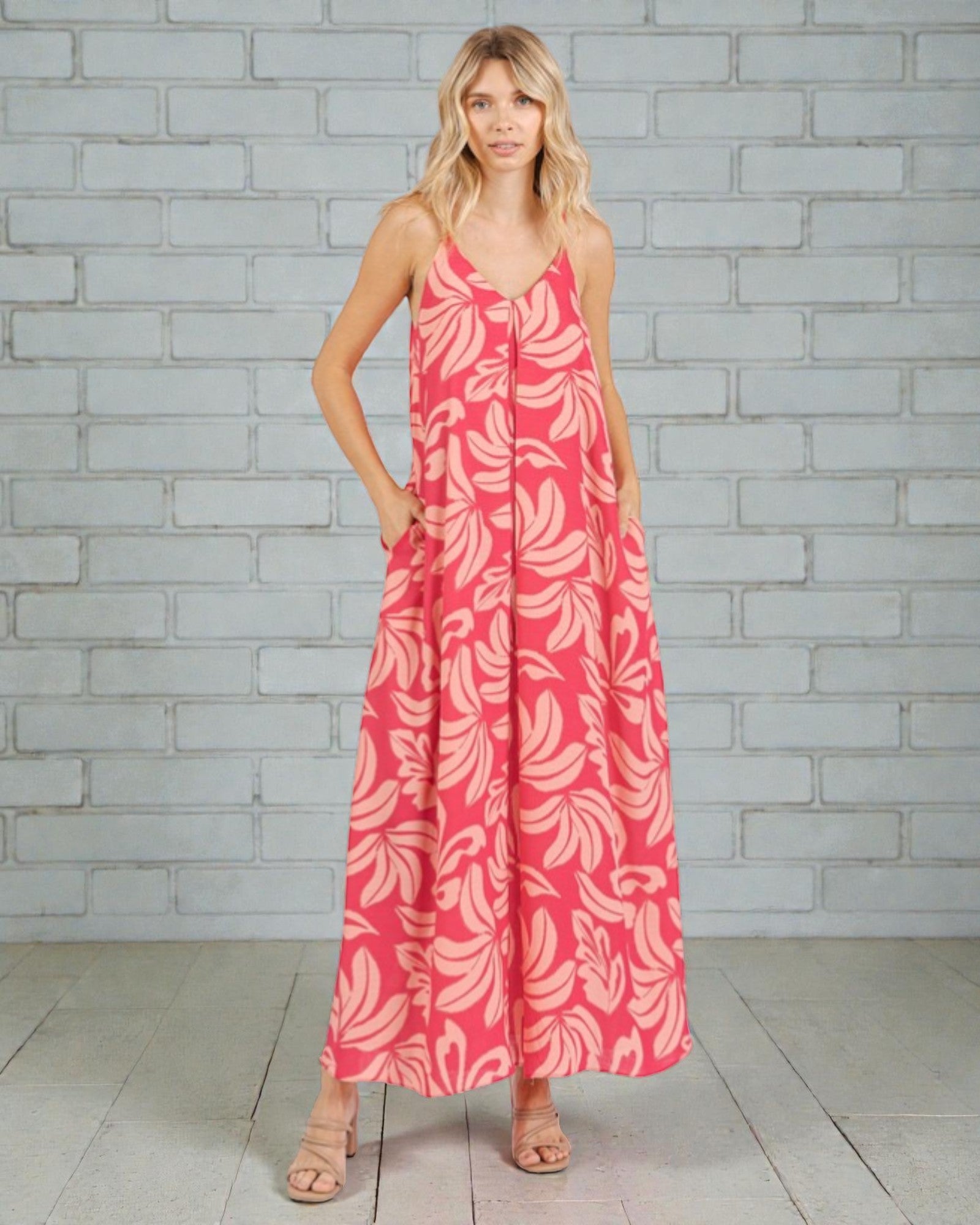 Woman wearing a pink floral dress against a gray brick wall.