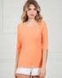 Woman wearing an orange long-sleeve top and white shorts against a light background