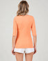 Person wearing an orange top and white shorts on a plain background